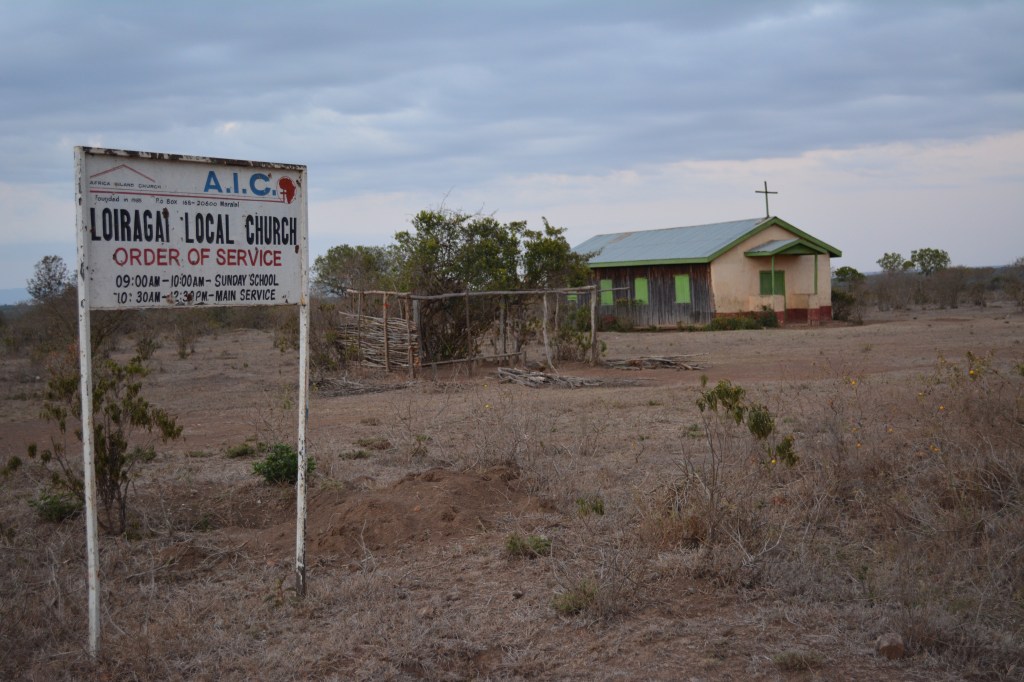 A picture of the front of the church.  In the foreground is the original site of the church, under a tree.  Many churches in remote Kenya meet under a tree until they can raise funds to build a building.  They left the original church there to remember where they came from.  Beautiful!
